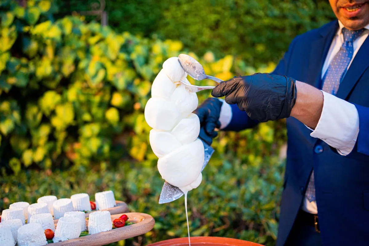 Il casaro solleva una treccia di mozzarella appena filata, con il verde del giardino dietro