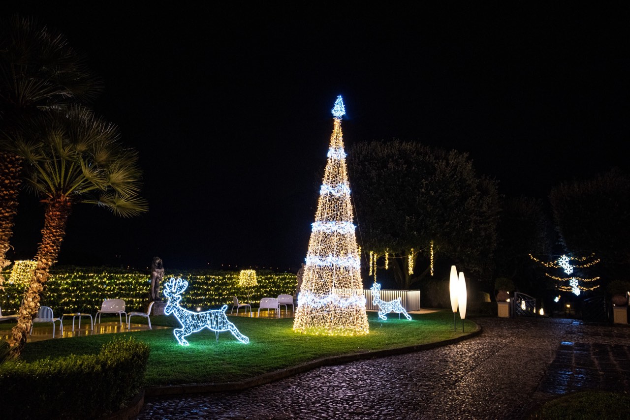 Albero di Natale luminoso alto nel parco di Villa Soglia con renne illuminate e palme