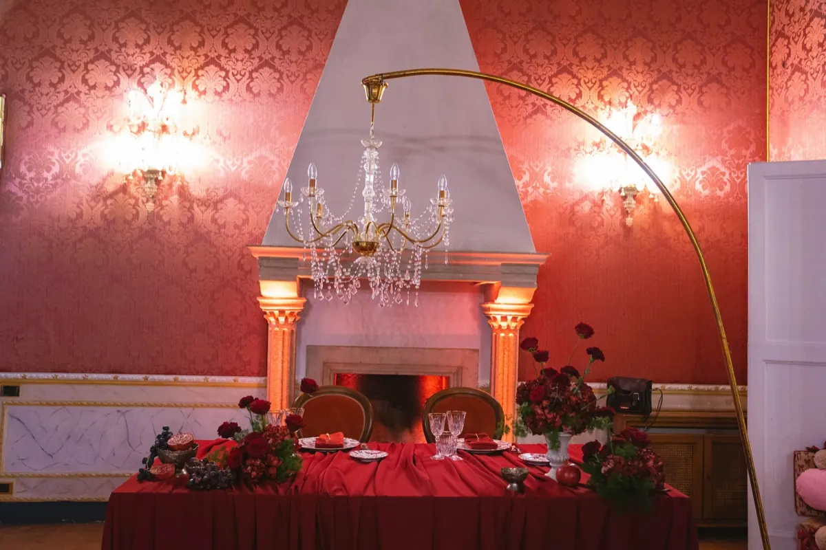 Sala damascata rossa con camino, lampadario di cristallo e tavolo apparecchiato in rosso