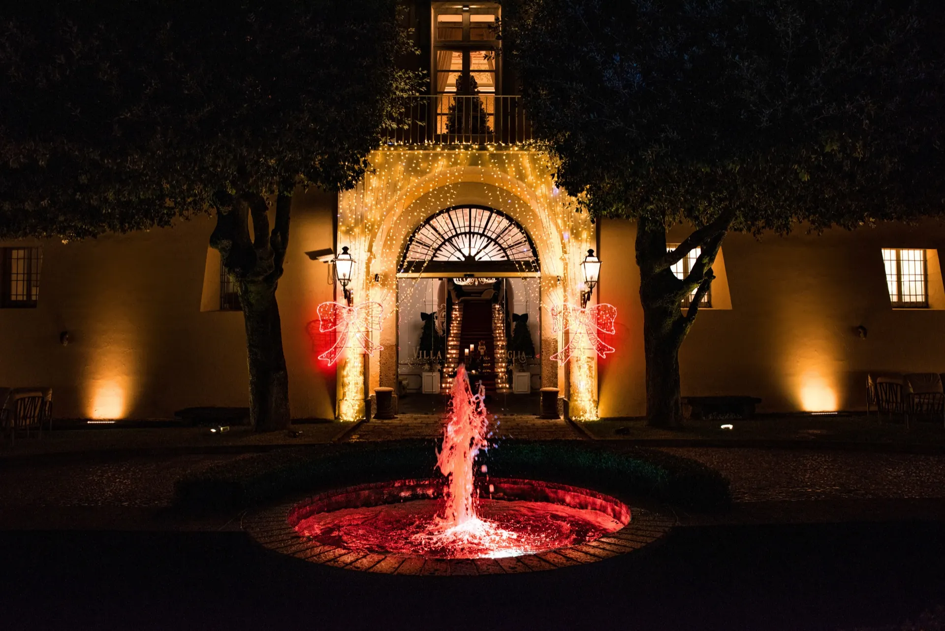 Fontana illuminata di rosso davanti all'arco della villa, nella notte di Natale