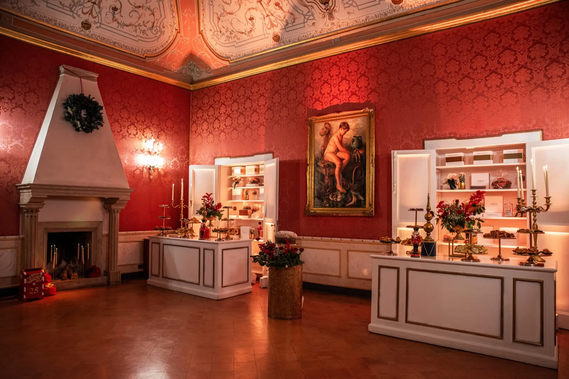 Salotto damascato rosso addobbato per Natale con camino, credenze e composizioni floreali