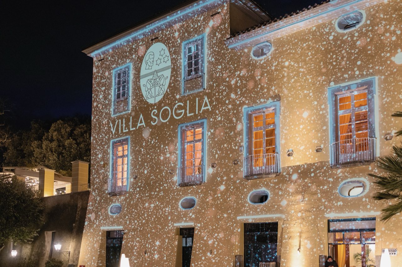 Facciata di Villa Soglia di notte con lo stemma e il nome proiettati fra le finestre illuminate