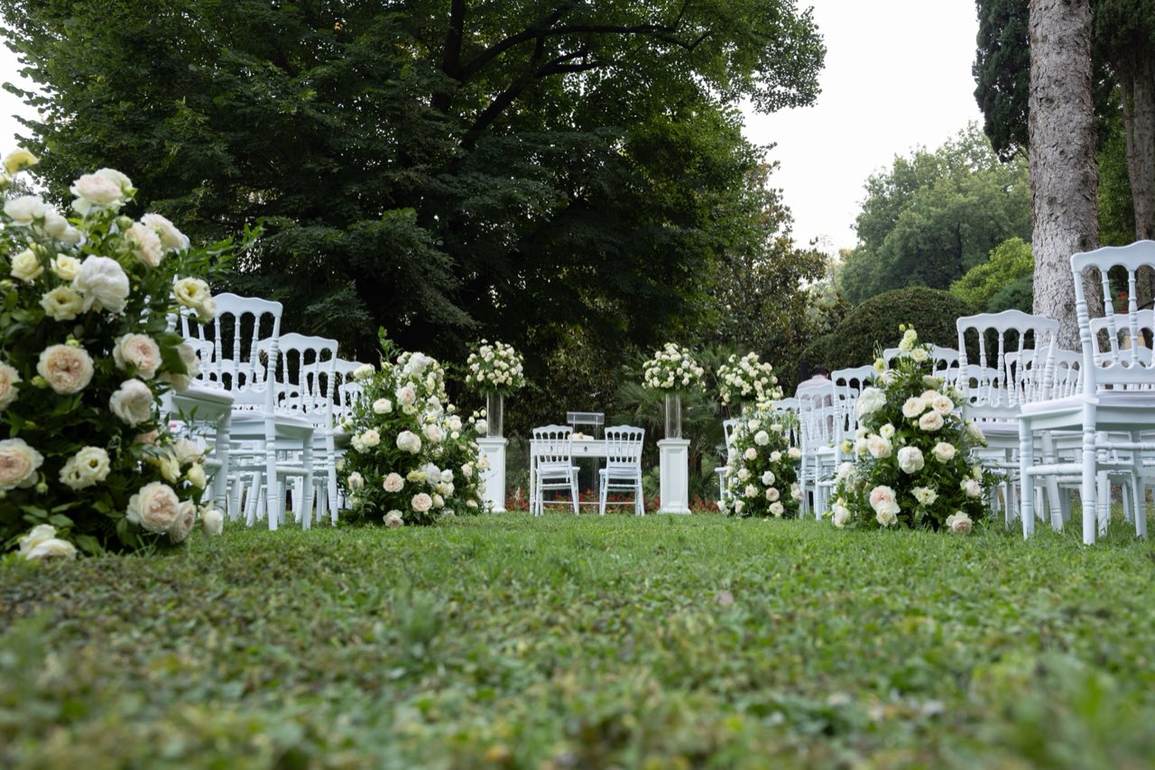 Rito civile allestito in giardino con sedute bianche e composizioni floreali