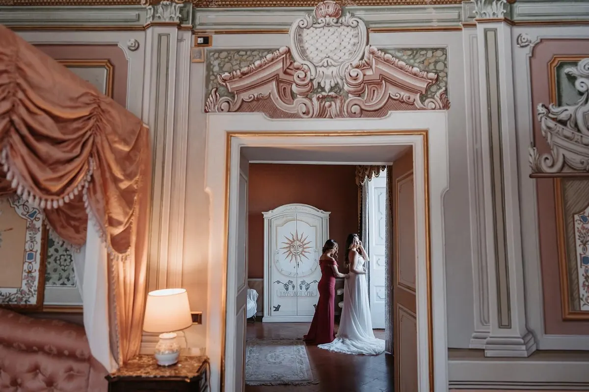 La sposa con una damigella sulla soglia della Suite, fra tendaggi rosa e porte dipinte