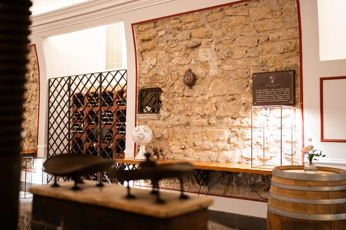Parete in pietra dell'Antica Scuderia con cantinetta a rombi, botte e banco illuminato
