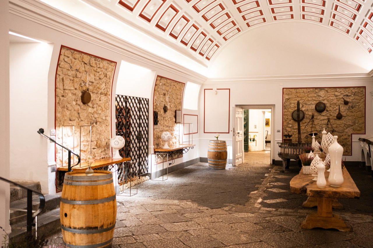 Veduta d'insieme dell'Antica Scuderia con pareti in pietra, botti di rovere e tavolo conviviale