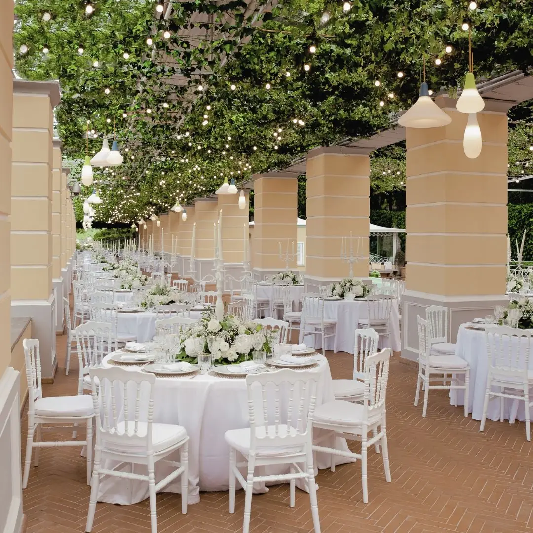 Tavoli rotondi sotto il colonnato della Sala Garden Glamour, fra pilastri ocra, rampicanti e luci sospese
