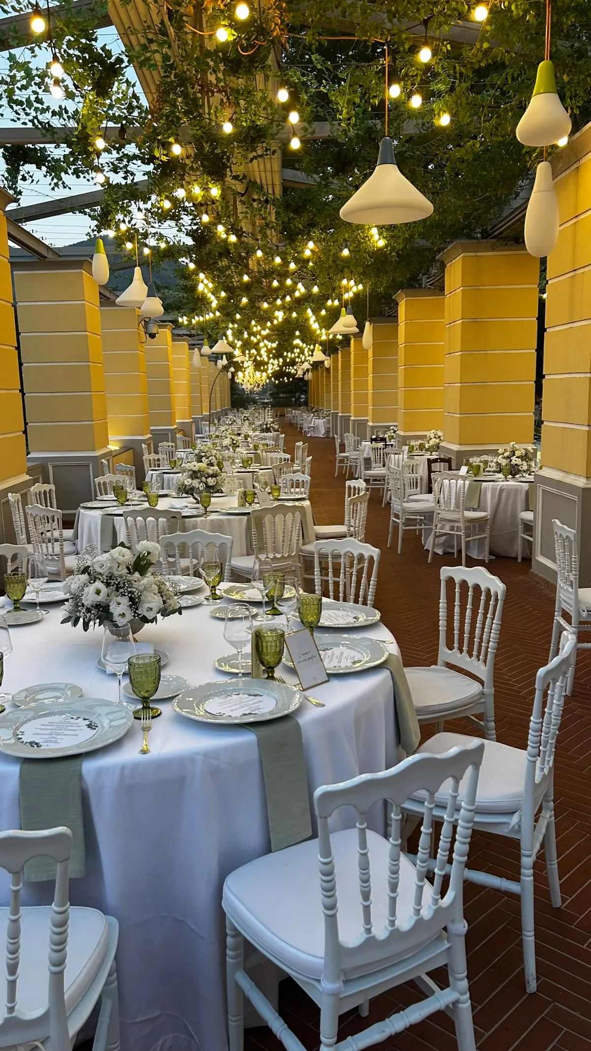 Il colonnato della Sala Garden Glamour in prospettiva, con i tavoli apparecchiati, le lampade a campana e le luci sospese
