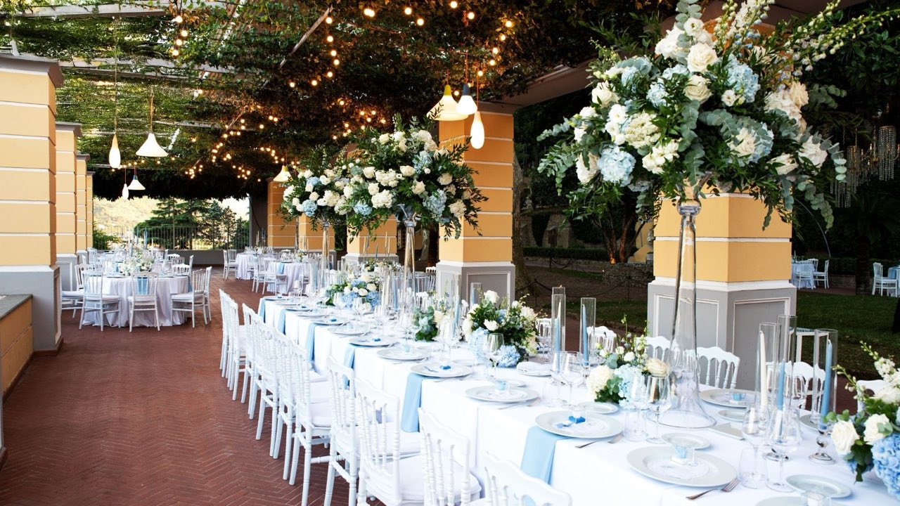 Tavolata imperiale con alti centrotavola di ortensie e rose sotto il pergolato illuminato della Sala Garden Glamour