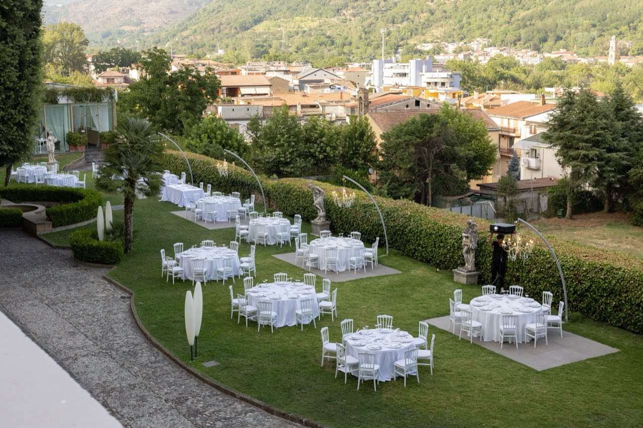 Cena in giardino con tavoli rotondi, statue e lampadari sospesi ad arco