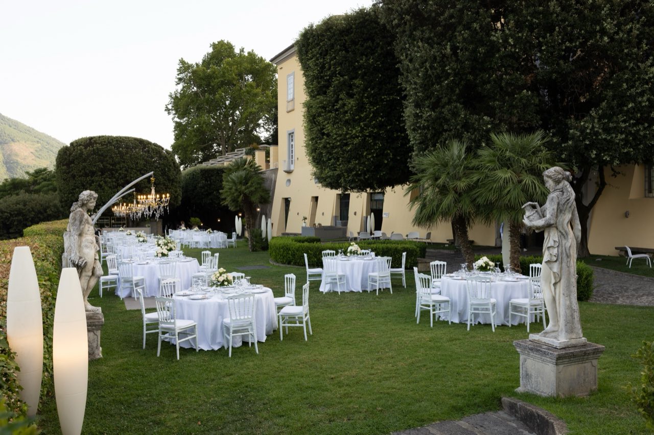 Allestimento in giardino davanti alla facciata ocra della villa, tra topiaria e statue