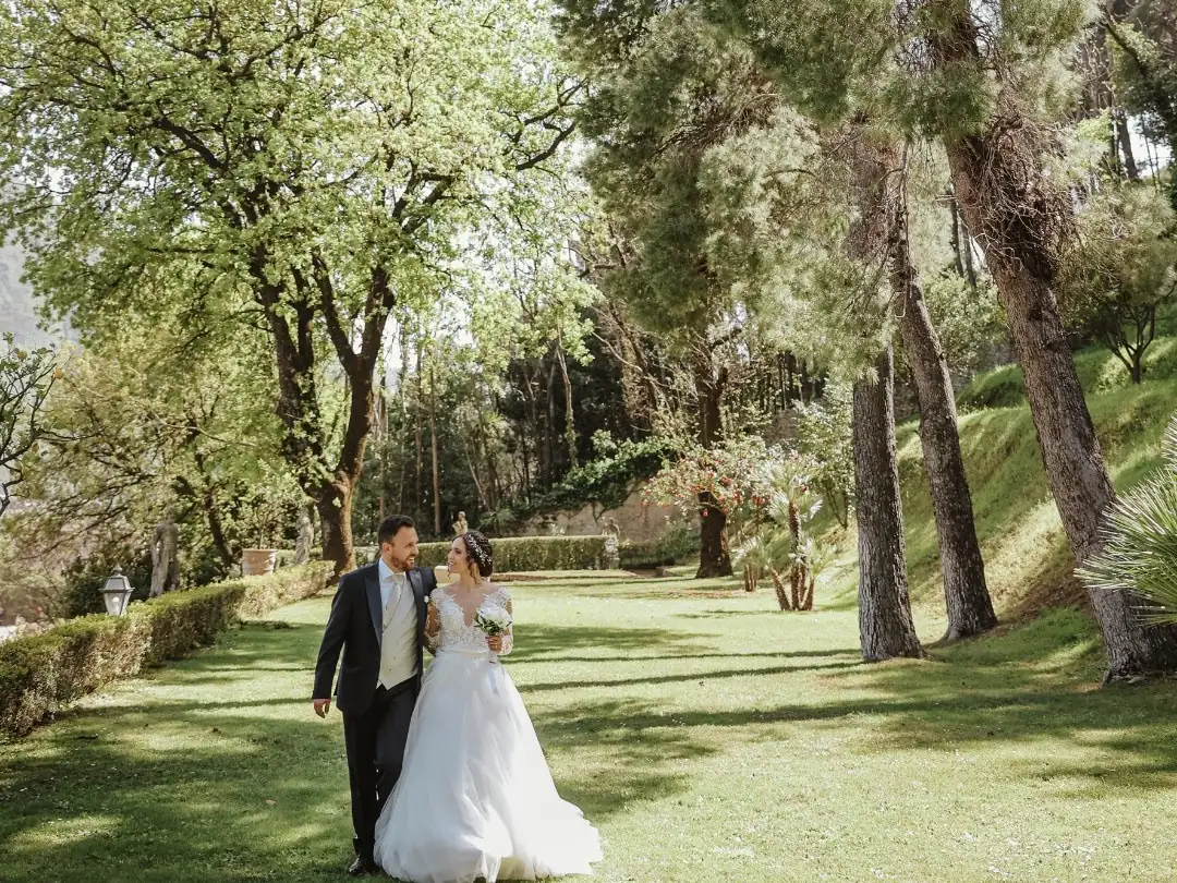 Sposi a passeggio sul prato del parco, fra alberi secolari e siepi