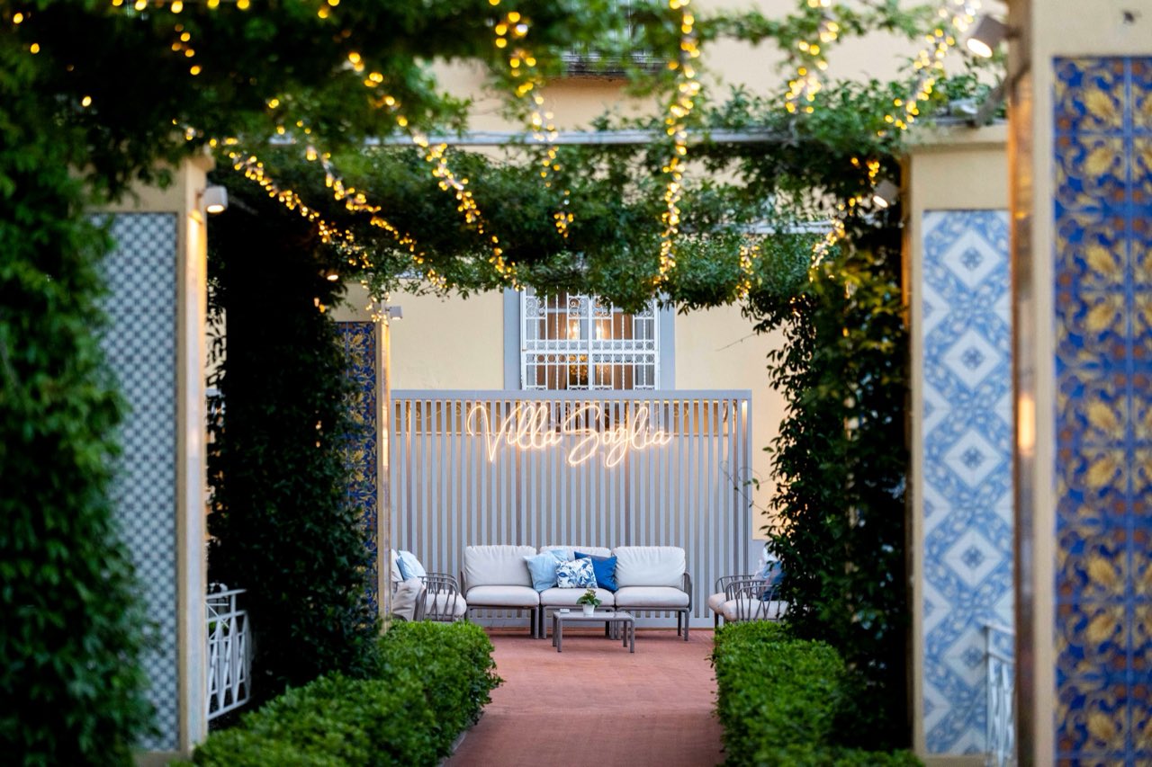 Lounge sotto la pergola con luci sospese, insegna Villa Soglia e pannelli di maioliche