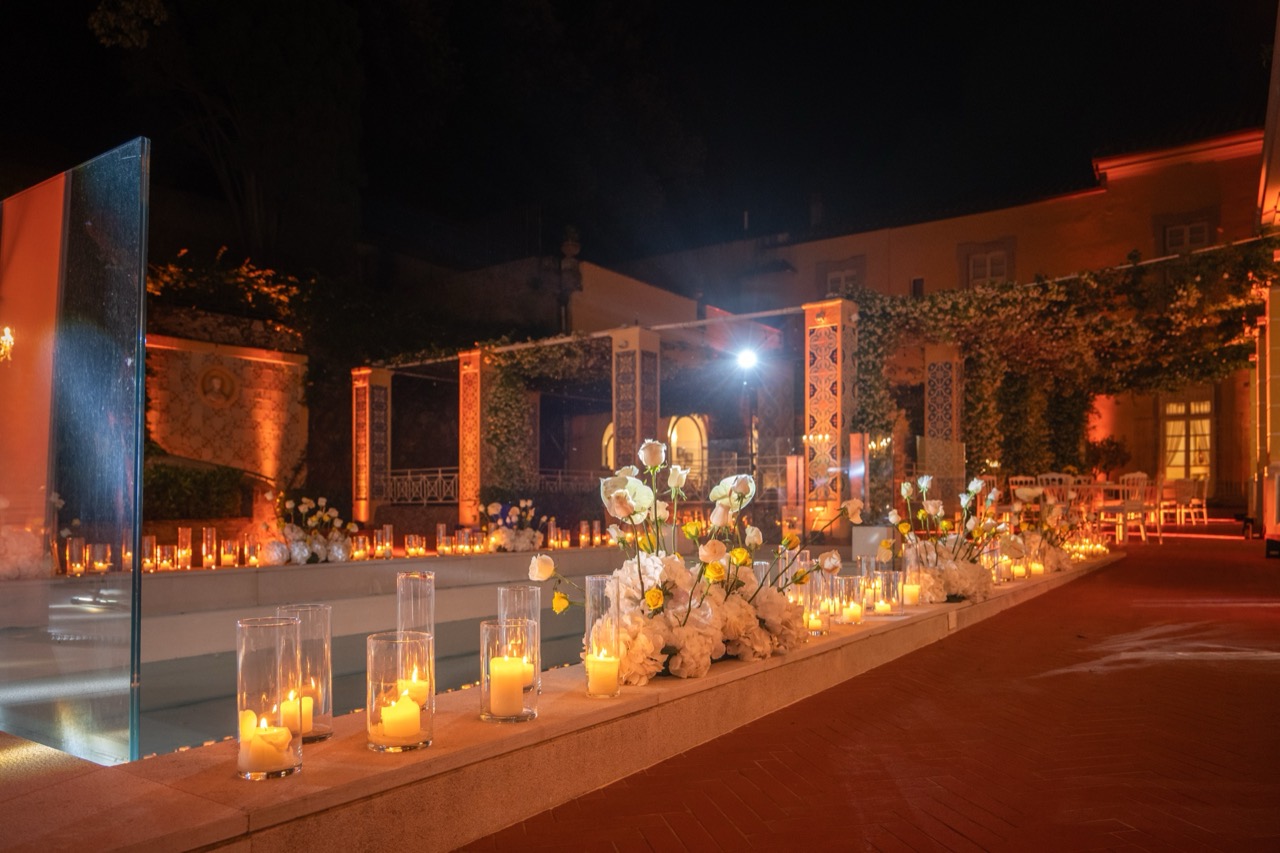 Piscina di notte con candele lungo il bordo e la facciata della villa illuminata