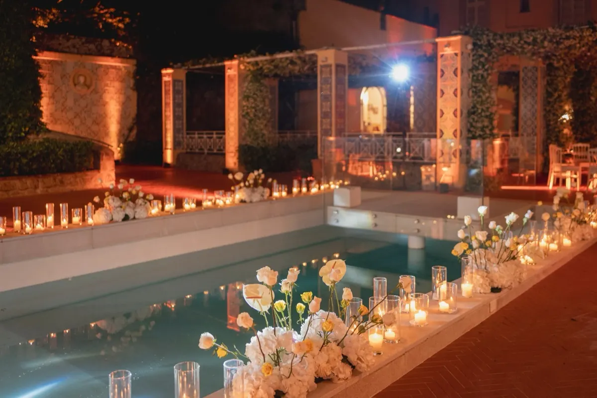Piscina di notte con rose bianche e candele lungo il bordo, davanti al colonnato di maioliche illuminato