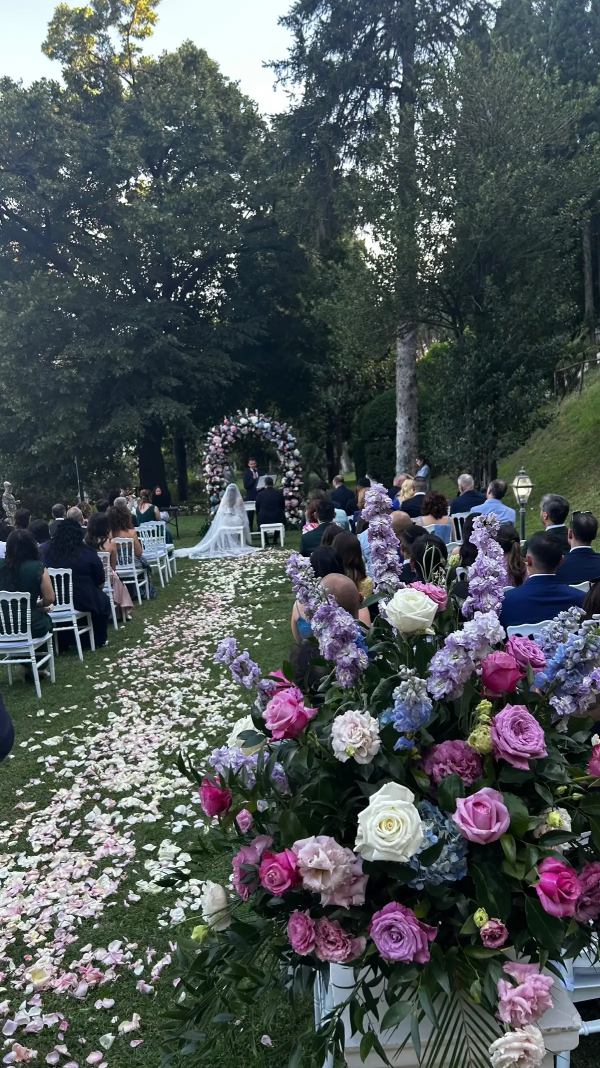 Navata coperta di petali con gli ospiti seduti e composizioni di rose e ortensie in primo piano