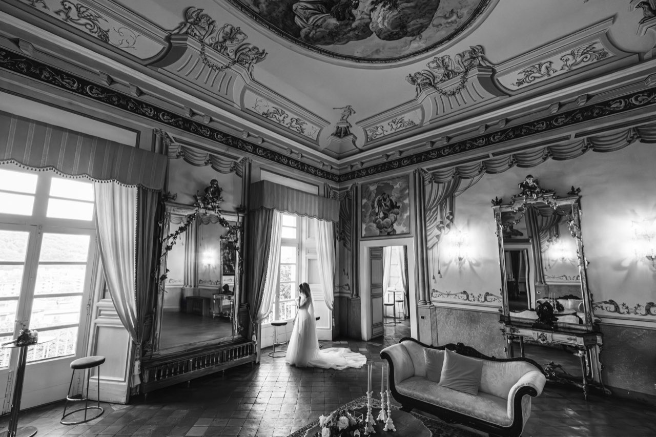 Salone affrescato in bianco e nero con grandi specchiere e la sposa alla finestra