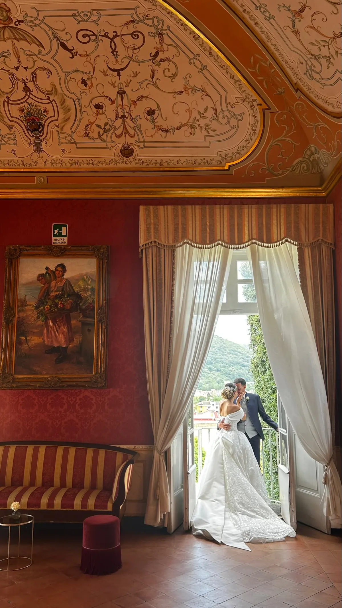 Sposi alla finestra del salotto rosso damascato, sotto il soffitto decorato