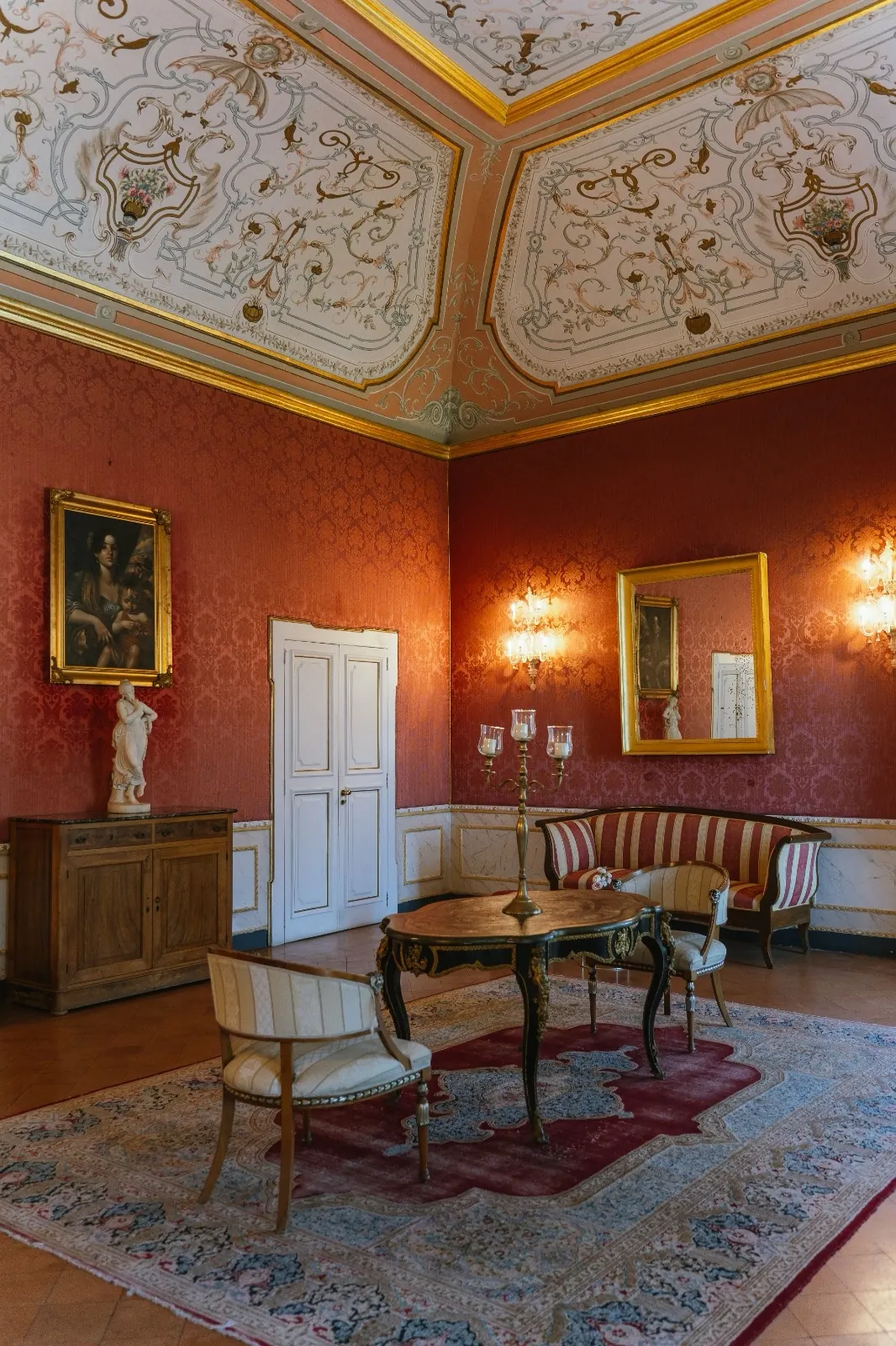 Salotto rosso damascato con soffitto decorato, poltrone, tavolino intarsiato e tappeto antico