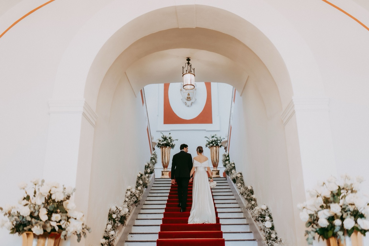 Scalone d'onore con passatoia rossa, vasi dorati di rose bianche e stemma di famiglia