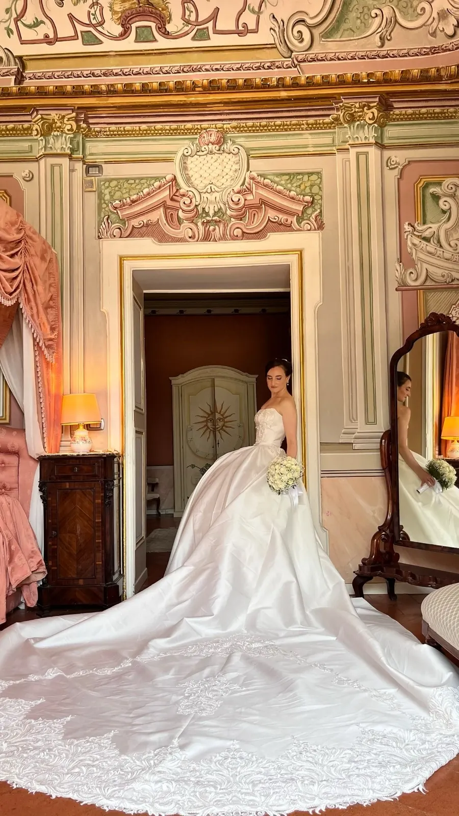 Sposa con il lungo strascico sulla soglia della suite storica, fra pareti decorate e stucchi