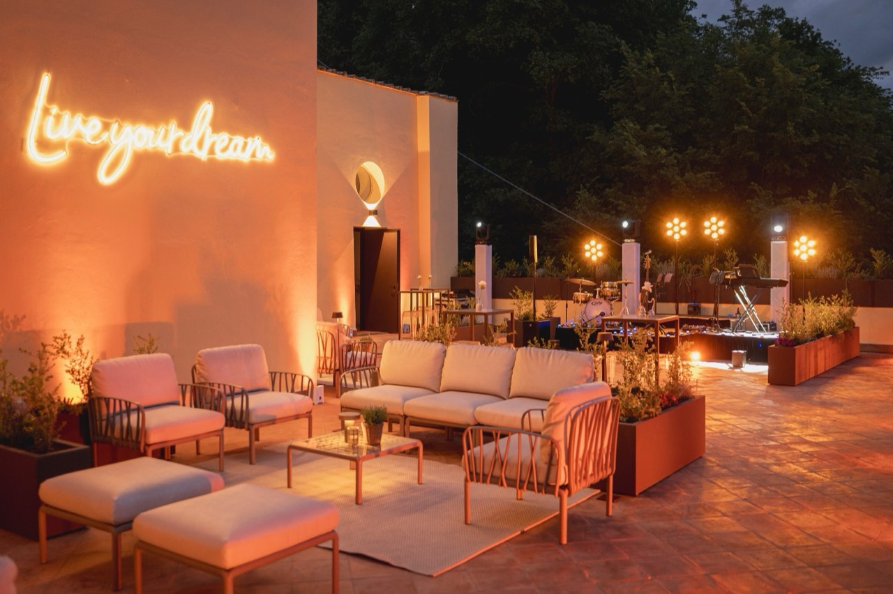 Terrazza bar di sera con divani, pouf e l'insegna al neon Live your dream accesa sul muro
