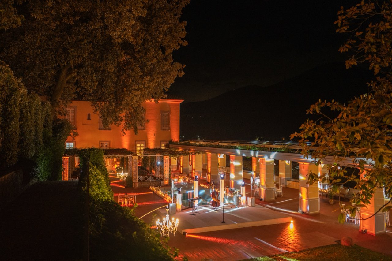 Veduta notturna d'insieme con colonnato ambrato, palco della band e pista da ballo